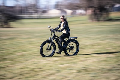白天，穿着黑色夹克的女人在绿草地上骑着黑色摩托车
